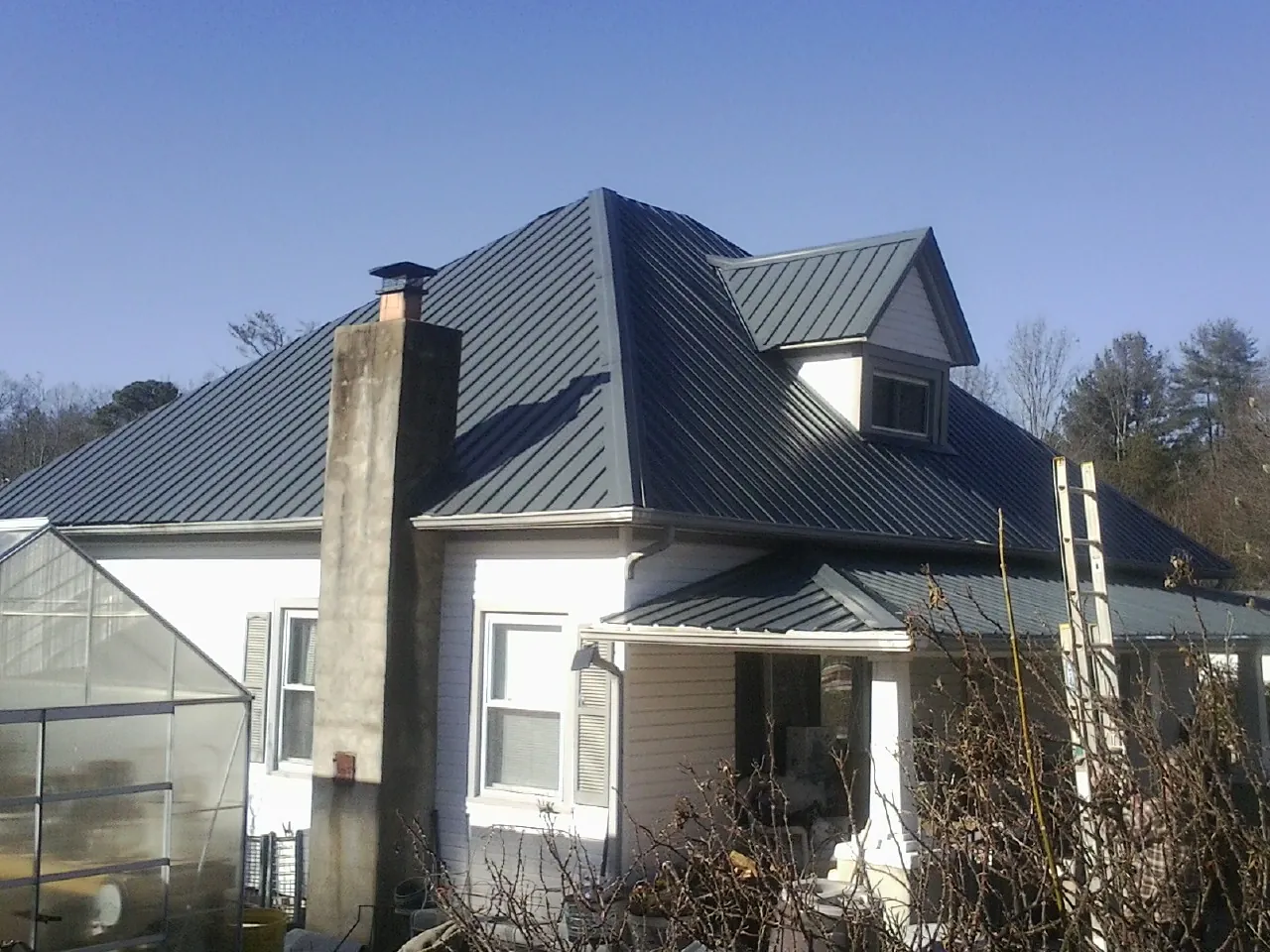 Dark blue standing seam metal roof on a white farmhouse with dormer — Slate & Tile Roof Repair by Roofing Brothers in Amory