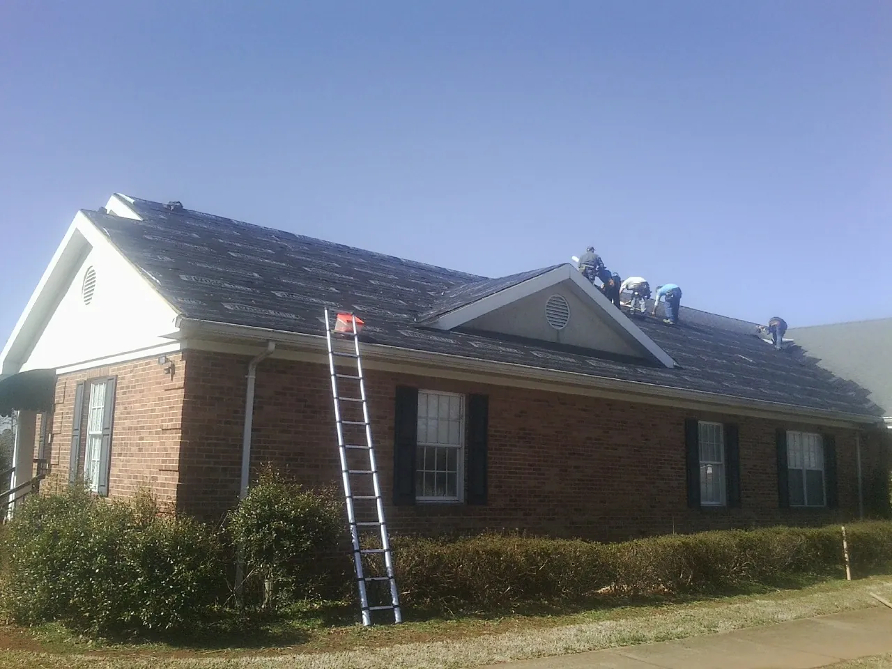 Crew tearing shingles off a brick ranch roof with a ladder set — Emergency Roof Repair work by our crew in Amory