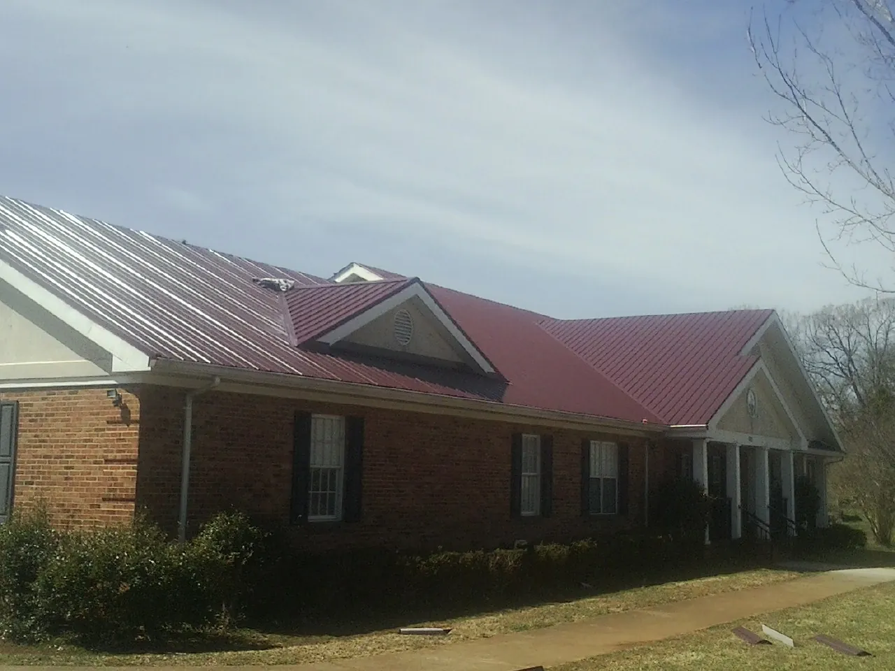 Red metal roof with gabled entries on a long brick building, from a Hail Damage Roof Repair job in Amory