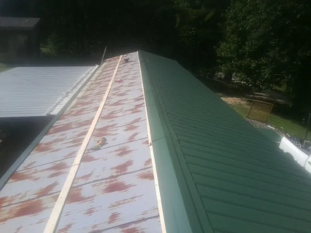 Old rusted panels beside newly installed green metal roofing — Wind Damage Roof Repair by Roofing Brothers in Amory