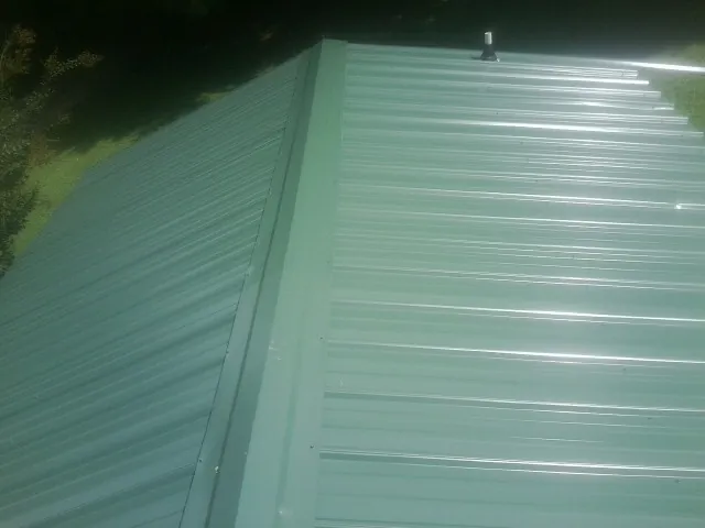 New green metal panels meeting at the ridge of a roof — Flat Roof Repair work by our crew in Amory