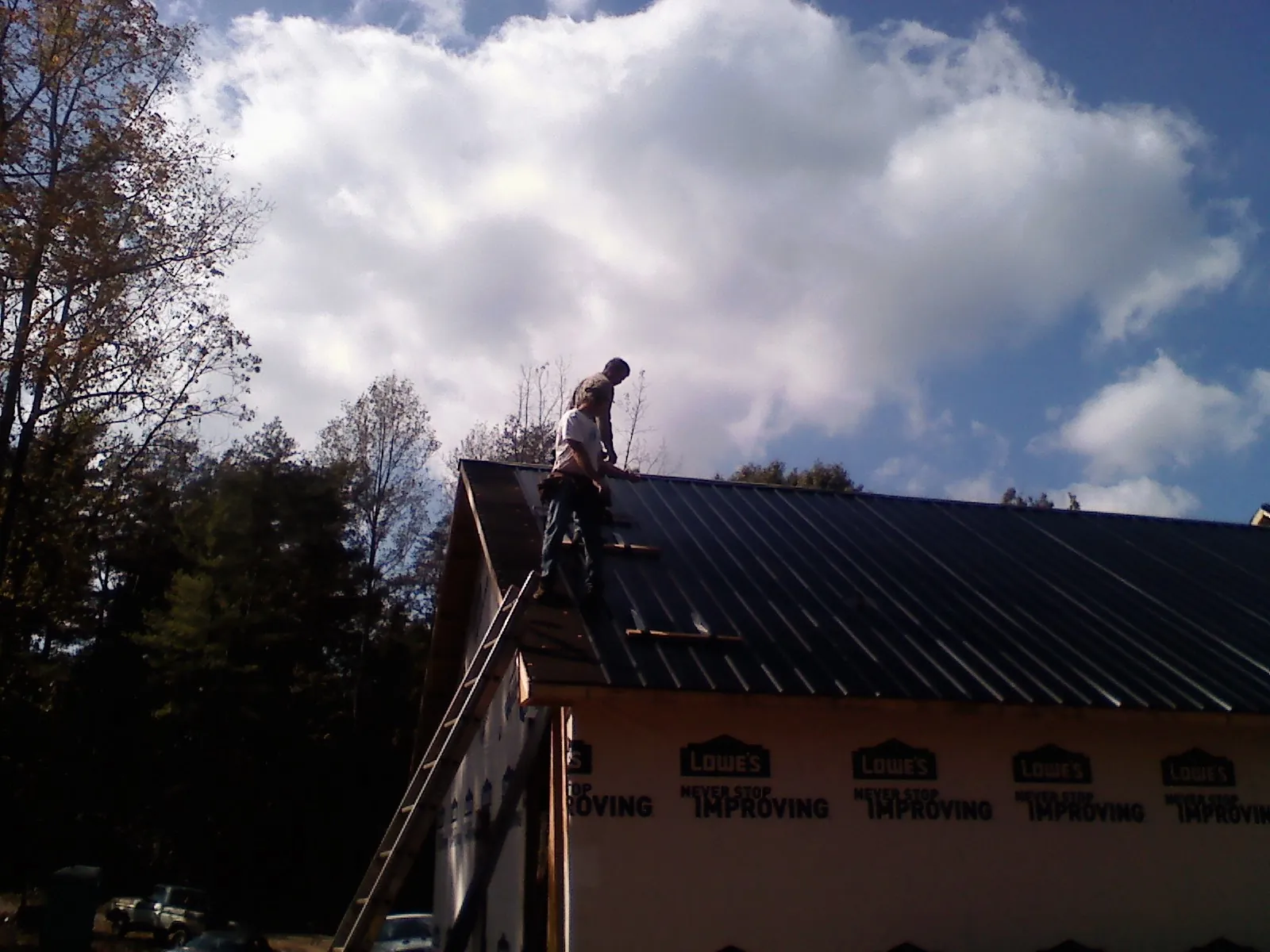 Roofer fastening dark metal panels high against a cloudy sky, from a Roof Inspection job in Amory